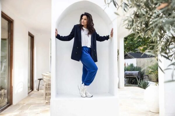 Vrouw met zwarte jas, witte bloes, blauwe joggingsbroek en witte sneakers