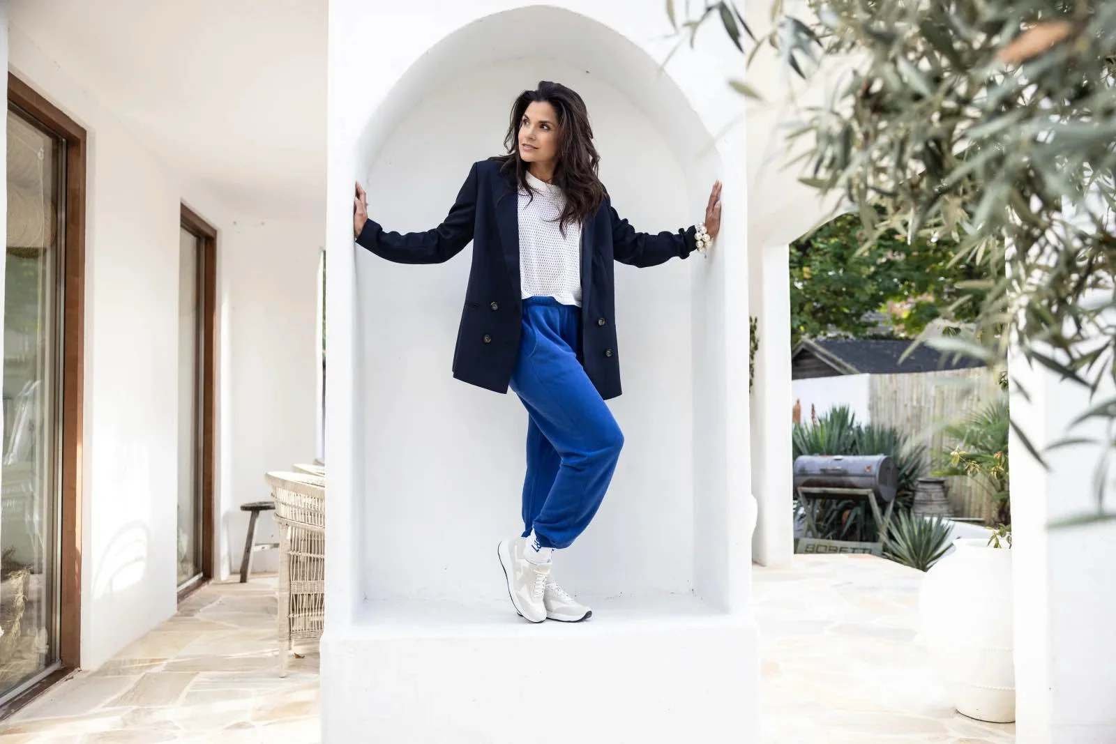 Vrouw met zwarte jas, witte bloes, blauwe joggingsbroek en witte sneakers